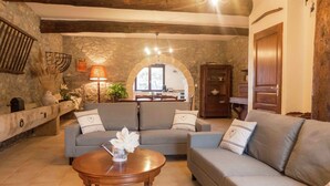 Un soggiorno accogliente con una parete in pietra, soffitto in legno, un divano, un tavolino da caffè e un'area pranzo sullo sfondo.
