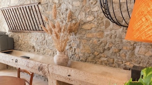 Un muro in pietra con una panca rustica, una sedia di legno e un vaso con piante essiccate.