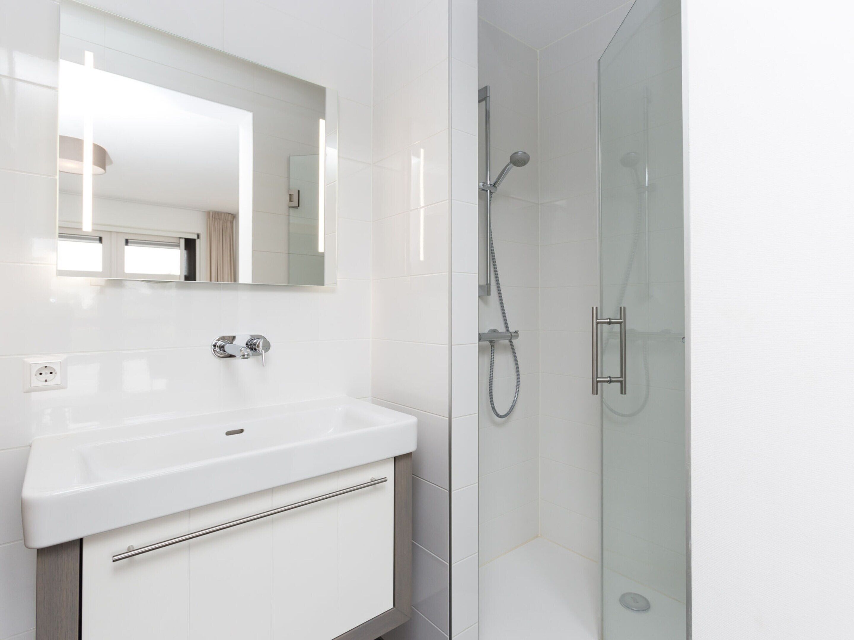 A modern bathroom with a white sink, a mirror, and a glass-enclosed shower area.