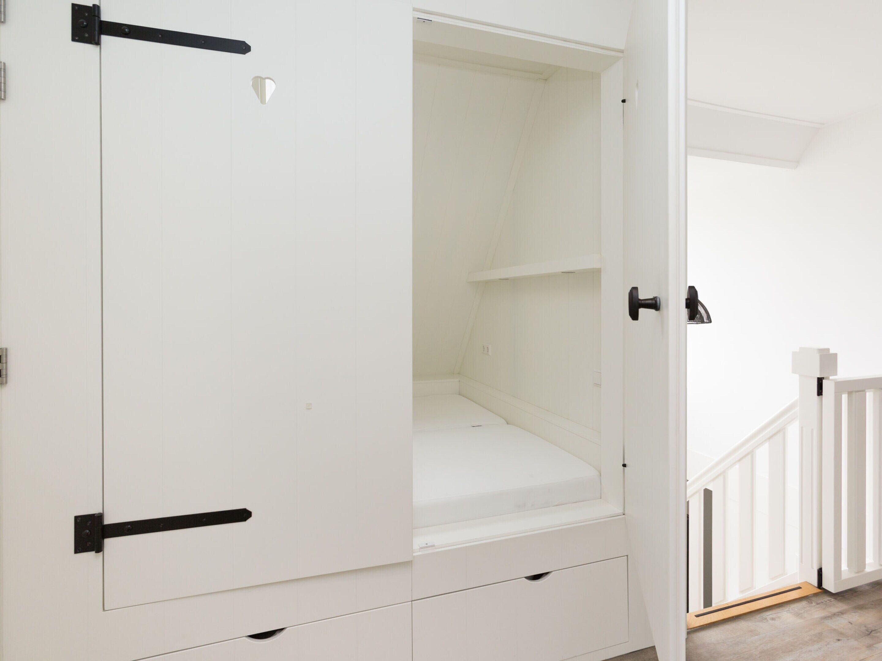 A white wardrobe with black handles and a small mirror.