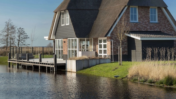 A house with a steeply pitched roof, large windows, and a dock extending into a body of water. - Friesland Villa With Fireplace (Delfstrahuizen)