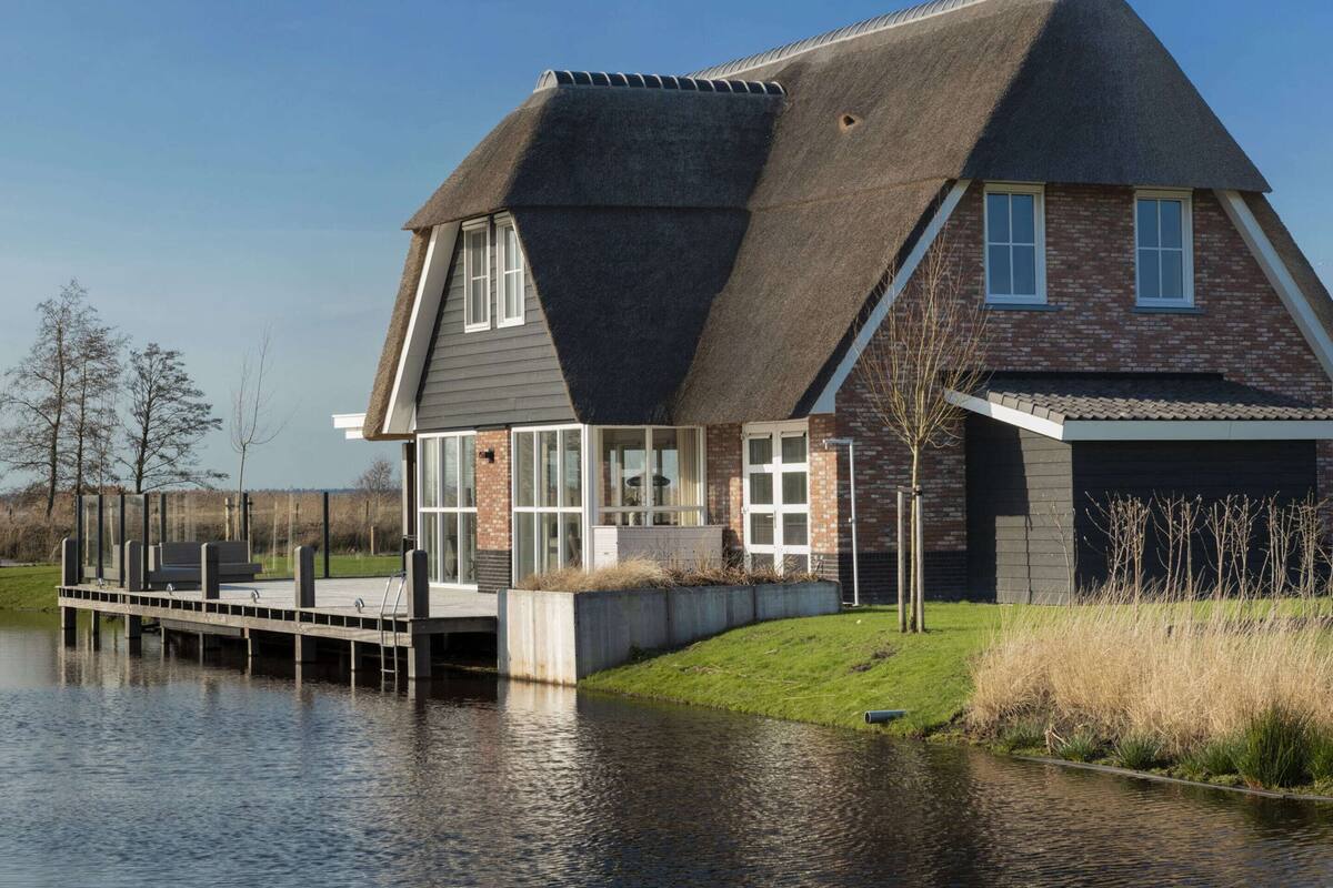 A house with a steeply pitched roof, large windows, and a dock extending into a body of water.