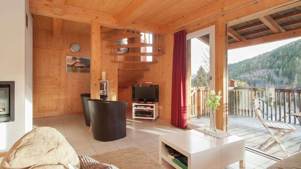 A wooden interior with a TV, seating, and a balcony with a view of the mountains. - Chalet in Styria Near the ski Area (Stadl-Predlitz)