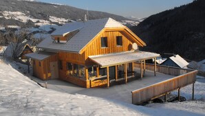 A wooden chalet with a balcony and a covered deck, surrounded by snow-covered hills. - Chalet in Styria Near the ski Area (Stadl-Predlitz)