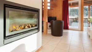A modern living room with a fireplace, wooden ceiling, and a view of the outdoors. - Chalet in Styria Near the ski Area (Stadl-Predlitz)