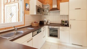 A modern kitchen with white cabinetry, stainless steel appliances, a wooden ceiling, and a window with a view of the outside. - Chalet in Styria Near the ski Area (Stadl-Predlitz)