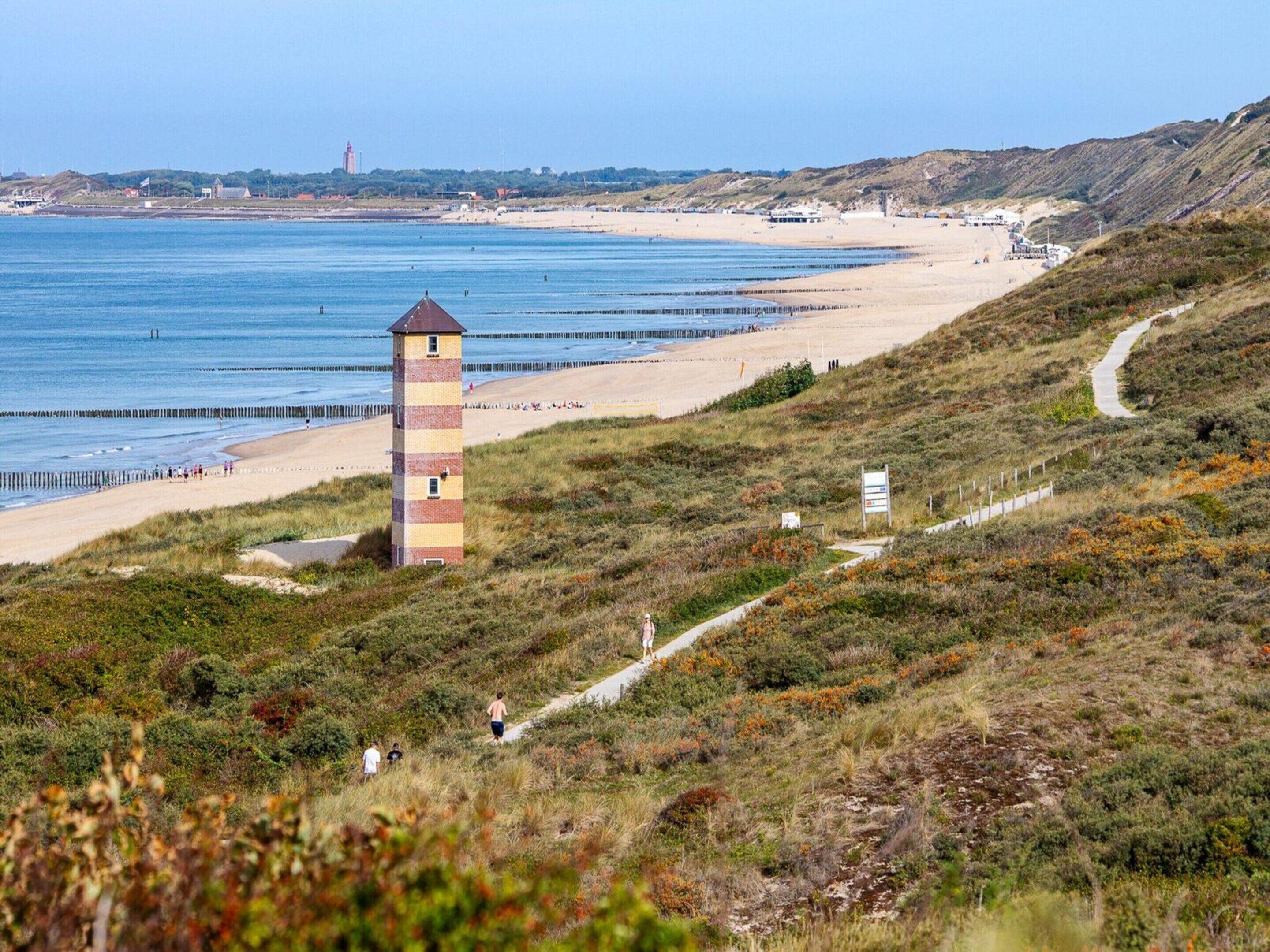 A coastal landscape with a lighthouse, beach, and grassy terrain.