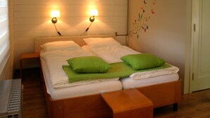 A double bed with green pillows, a wooden bench, and two wall-mounted lamps.