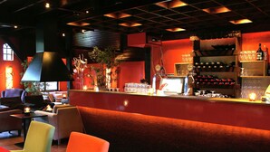 A bar area with seating, a counter with a computer, and shelves with bottles and glasses.