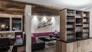Un salon moderne avec un mur d’accent en bois, un canapé noir, un meuble en bois contenant de la verrerie, et un coin repas avec une table et des chaises.