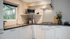 A modern kitchen with white cabinets, a stainless steel sink, a microwave, a gas stove, and a window with a view of trees.