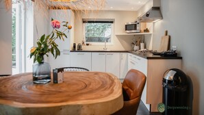 A modern kitchen with white cabinets, a wooden dining table, and a hanging light fixture.