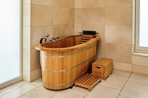 A wooden bathtub with a faucet and a wooden step leading into it, placed in a bathroom with tiled walls and floor.