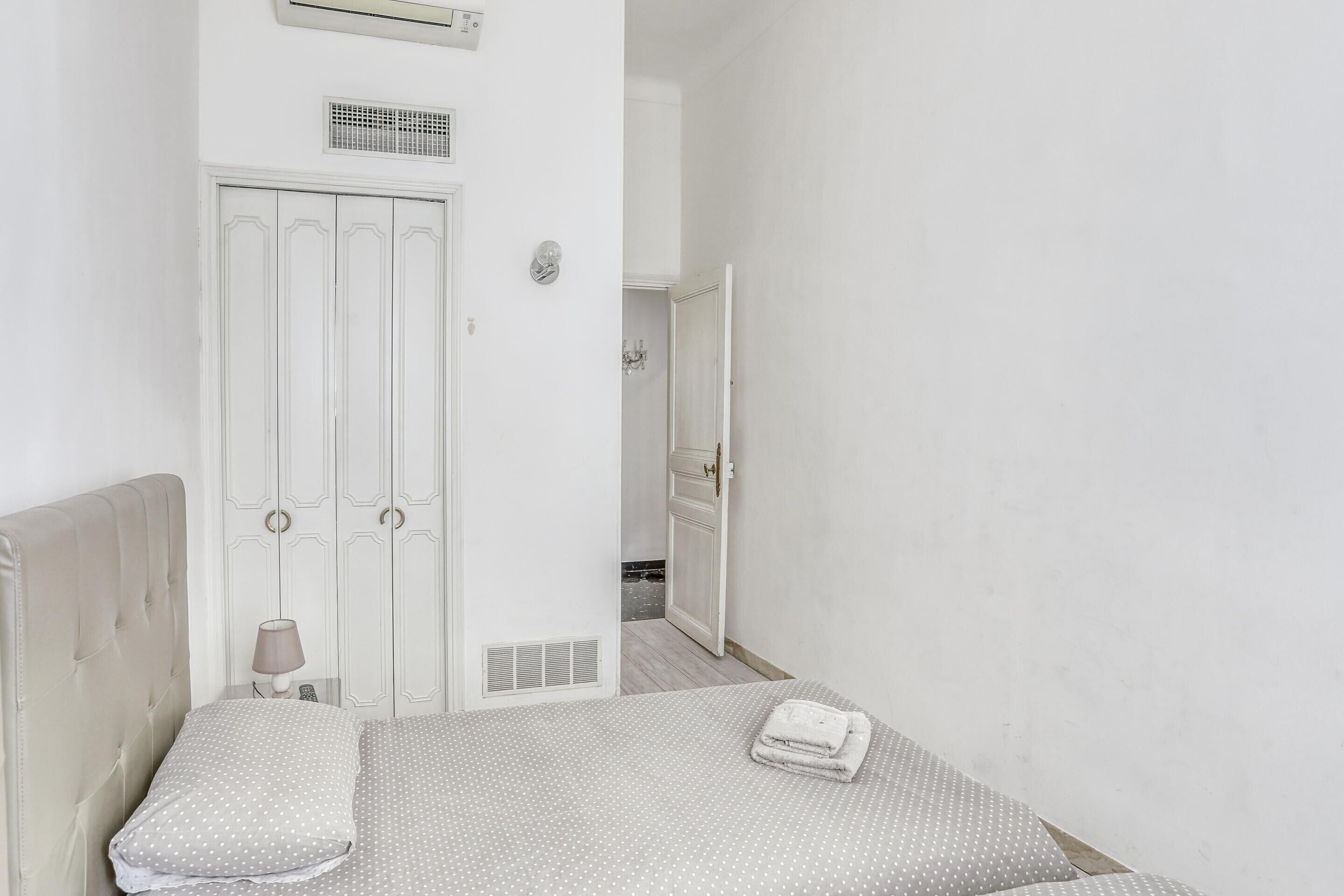 A bedroom with a bed, a nightstand, a lamp, a wardrobe, and a bathroom door.