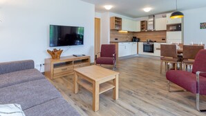 Una sala moderna con televisor de pantalla plana, muebles de madera y una zona de comedor con sillas y una mesa.