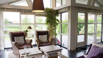 A spacious living area with large windows, wicker furniture, and a central plant.