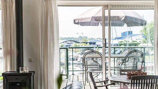 A balcony with a table and chairs, a sofa, and a large window with curtains. - Water Villa Kortgene by Veerse Meer (Kortgene)