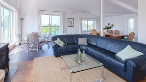 A spacious living area with a dark leather sofa, a glass coffee table, and a dining table with chairs. Large windows provide a view of the outdoors. - Water Villa Kortgene by Veerse Meer (Kortgene)