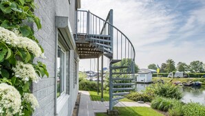 A spiral staircase leading to a second-floor balcony with a view of a marina and boats. - Water Villa Kortgene by Veerse Meer (Kortgene)
