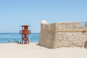 A stone building with a dome and a lifeguard tower on a beach.