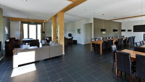 Ein geräumiger Raum mit hohen Decken, Holzbalken, einer großzügigen Sitzecke mit Sofas und einem Esstisch mit Stühlen.