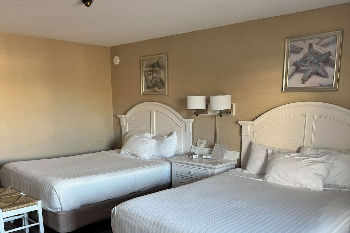 Ein Hotelzimmer mit zwei Einzelbetten, einem kleinen Tisch und zwei Nachttischlampen.