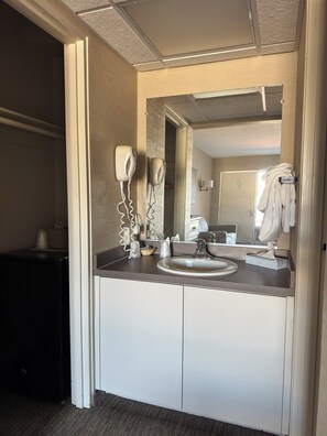 Un bagno moderno con uno specchio grande, un lavandino e un asciugacapelli. C'è un porta asciugamani con un asciugamano appeso, e un cesto sopra il ripiano.