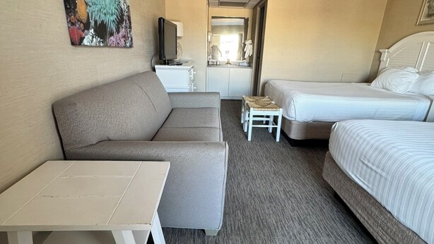 A hotel room with a sofa, a bed, a small table, a TV, and a bathroom visible through an open door. - Impala Island Inn (Ocean City)