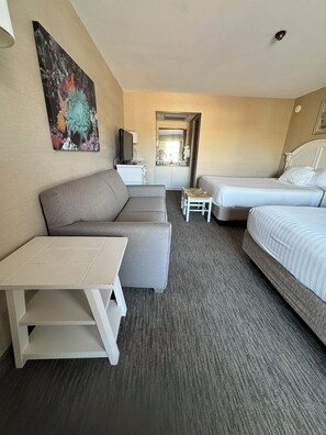 Ein Hotelzimmer mit Sofa, Bett, einem kleinen Tisch, einem Fernseher und einem sichtbaren Badezimmer durch eine geöffnete Tür.