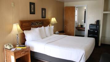 Hotelkamer met een bed, bedlampjes, een nachtkastje met een telefoon, een bureau met een magnetron en een deur naar een andere kamer.