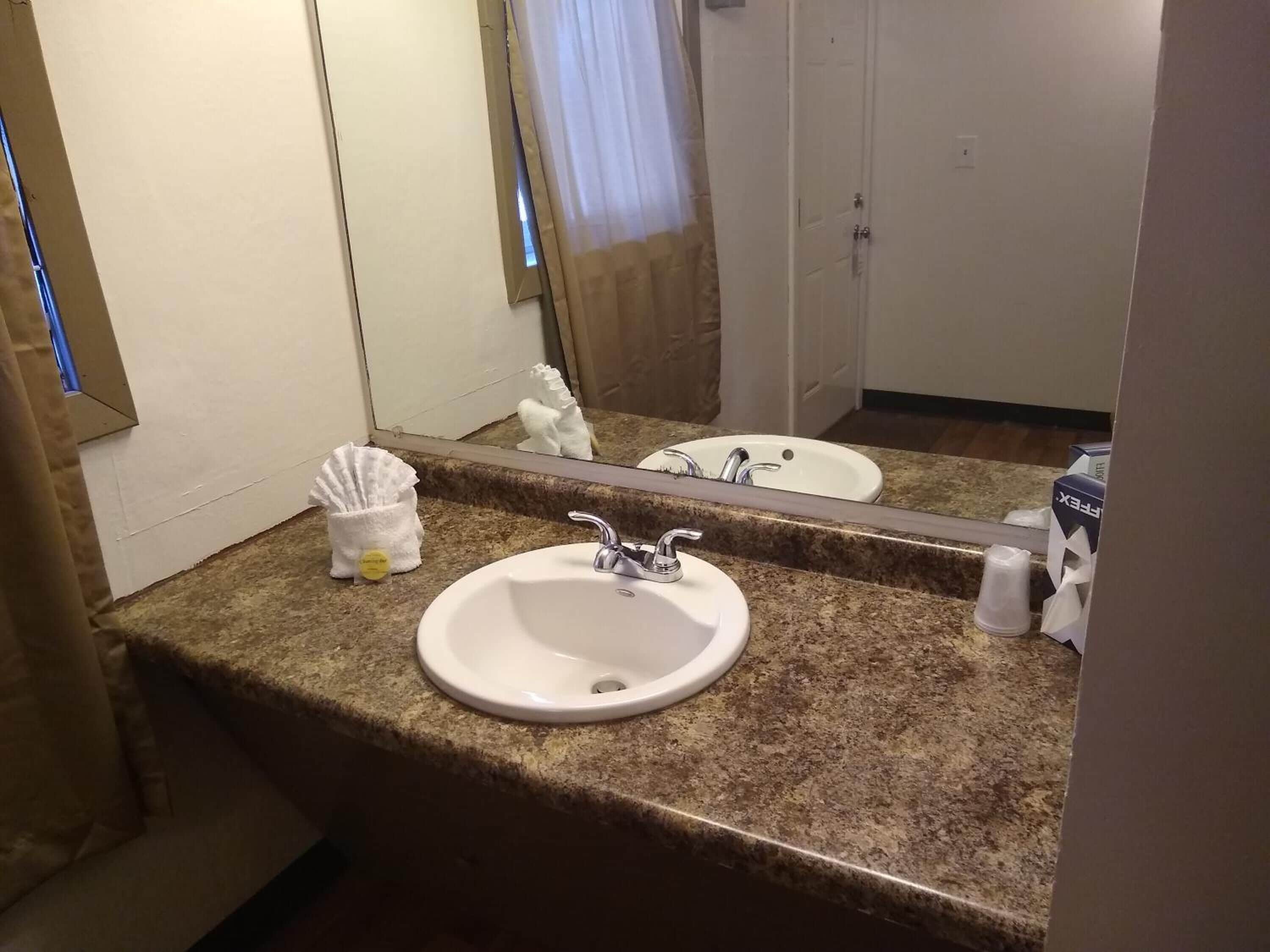 A bathroom with a granite countertop, a white sink, a mirror, and a towel dispenser.