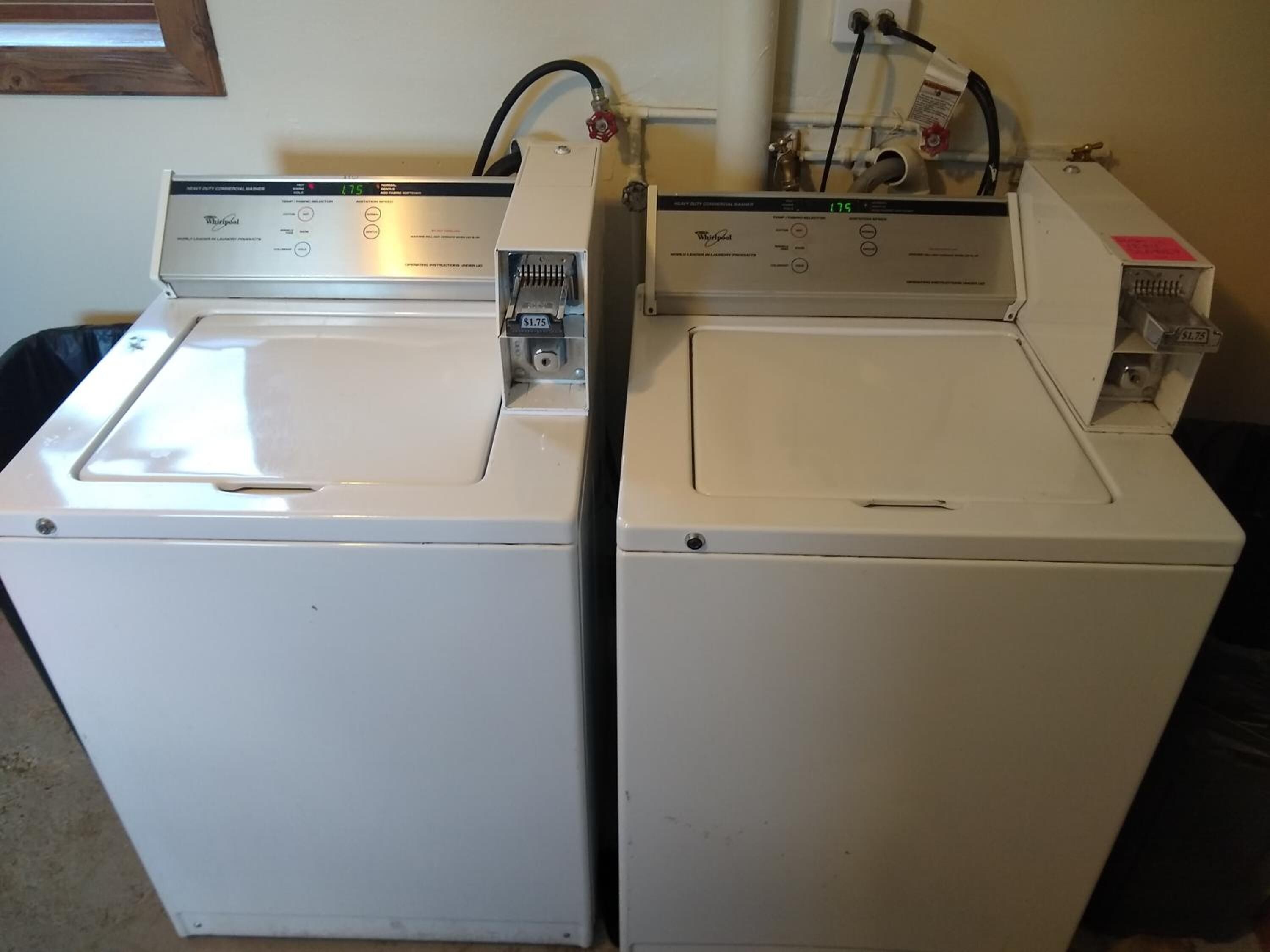 Two front-loading Whirlpool washers with control panels, hoses, and a water inlet valve.