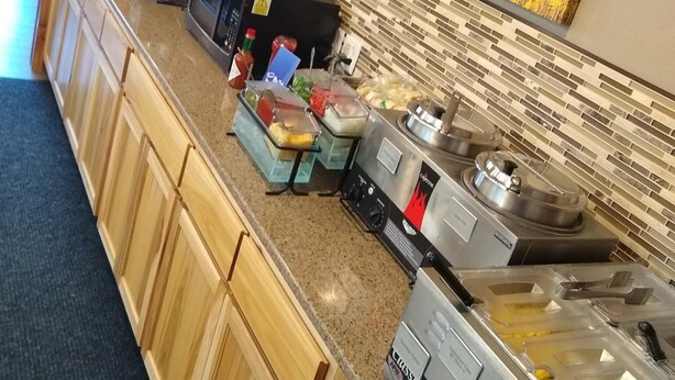 A kitchen area with wooden cabinets, a microwave, a coffee maker, and a food display. - Townhouse Motel (Lusk)