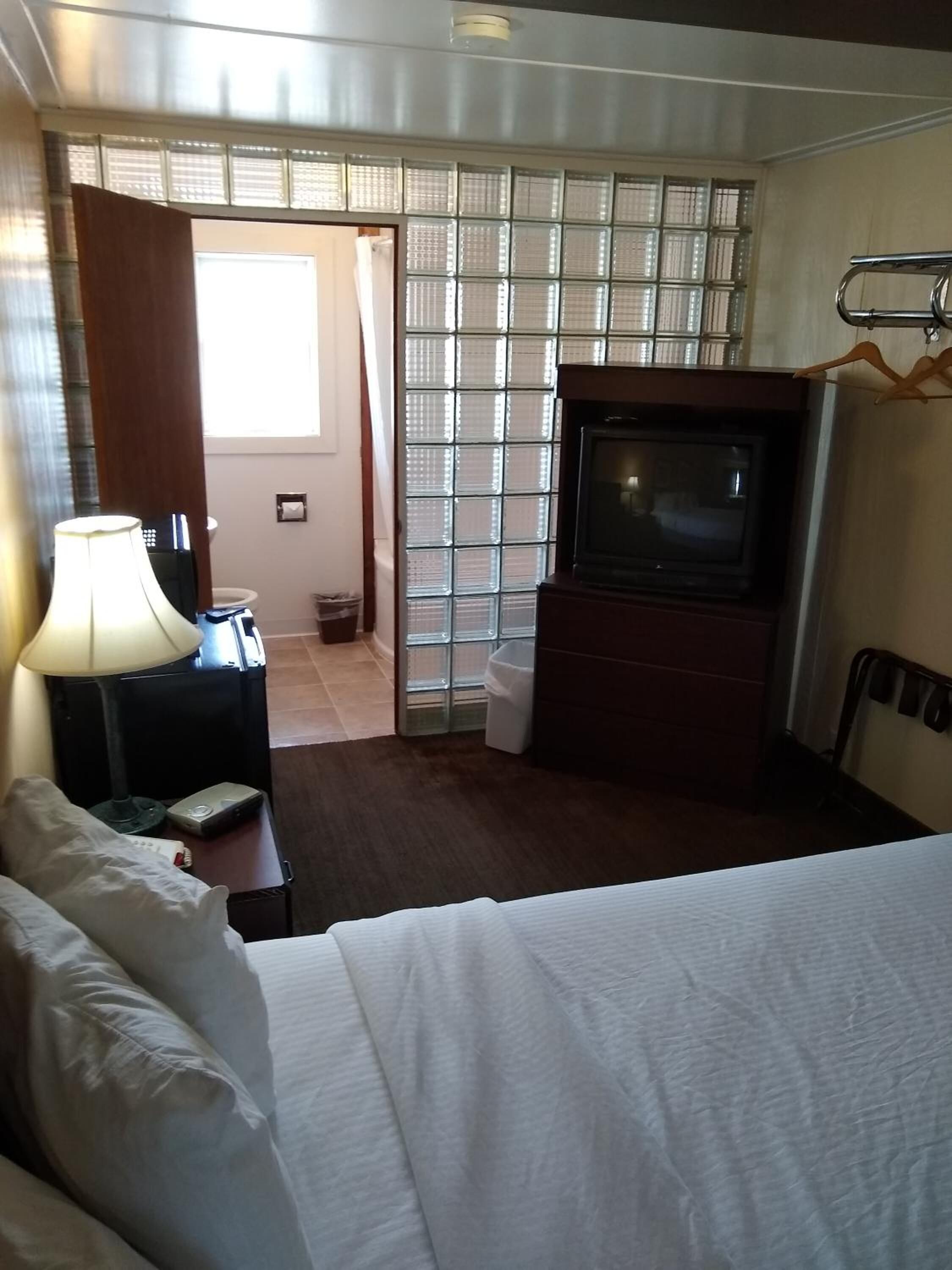 Una camera d'albergo con un letto, una televisione, una scrivania con una lampada e una finestra con persiane.