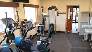 A gym with cardio machines, weightlifting equipment, and a television screen. - Townhouse Motel (Lusk)