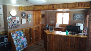 A kitchen with wooden cabinets, a microwave, a coffee machine, and a computer. There is a bulletin board with various items pinned to it. - Townhouse Motel (Lusk)