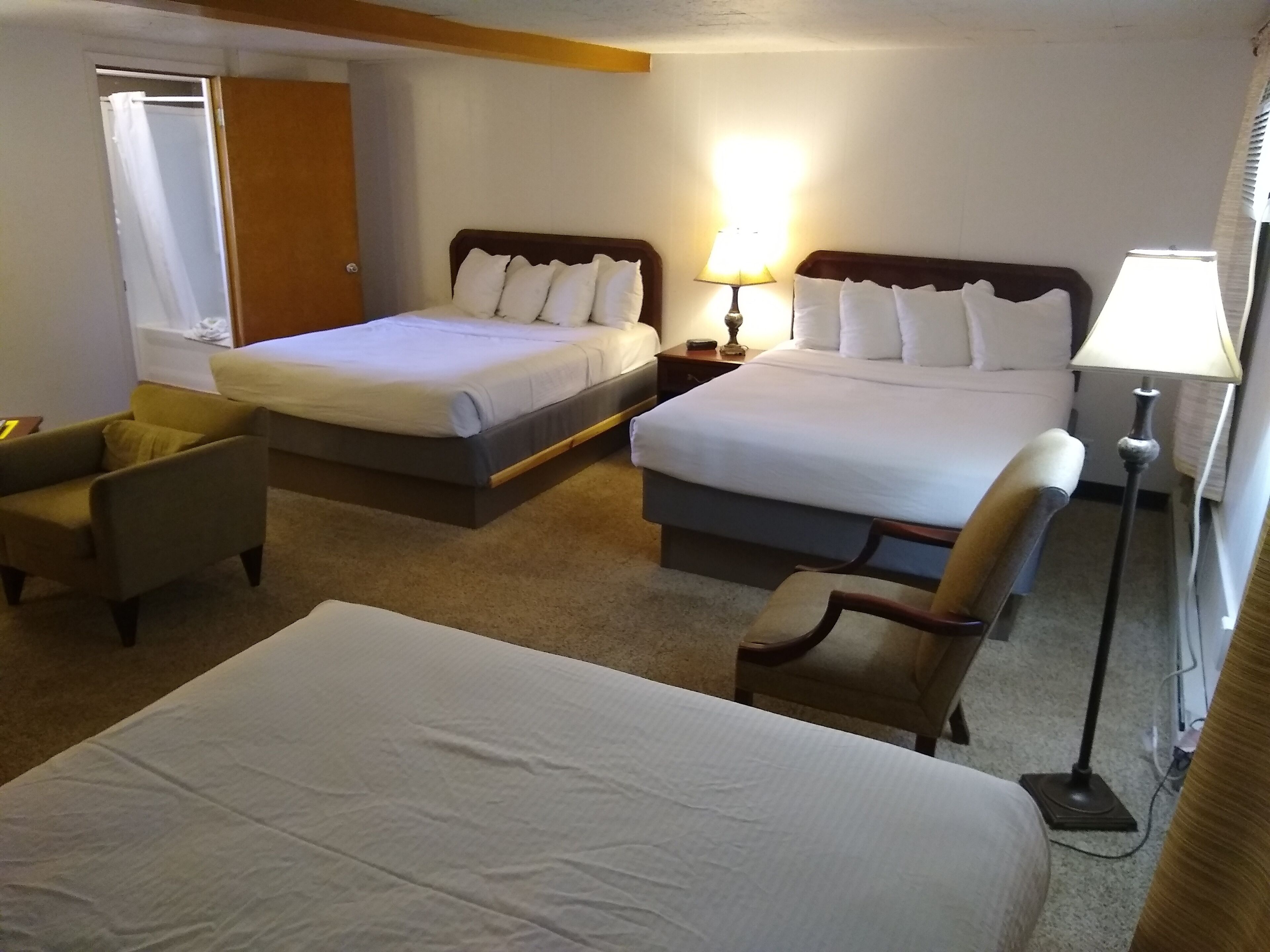 Habitación de hotel con dos camas, una zona de estar con una silla, una mesita de noche y una lámpara.