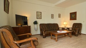 Una sala de estar con televisor, dos sofás de cuero, una mesa de centro de madera y un mueble de madera.