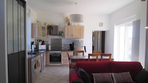 A compact kitchen with a dining area, a red sofa, and a large window. - Villa in Crux-la-ville Near Morvan Park (Crux-la-Ville)