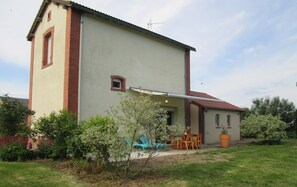 A two-story building with a flat roof, a small window, and a door. There is a patio with outdoor furniture and a potted plant. - Villa in Crux-la-ville Near Morvan Park (Crux-la-Ville)