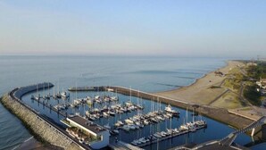Un port de plaisance où sont amarrés de nombreux bateaux, un petit bâtiment et une vue dégagée sur la côte.