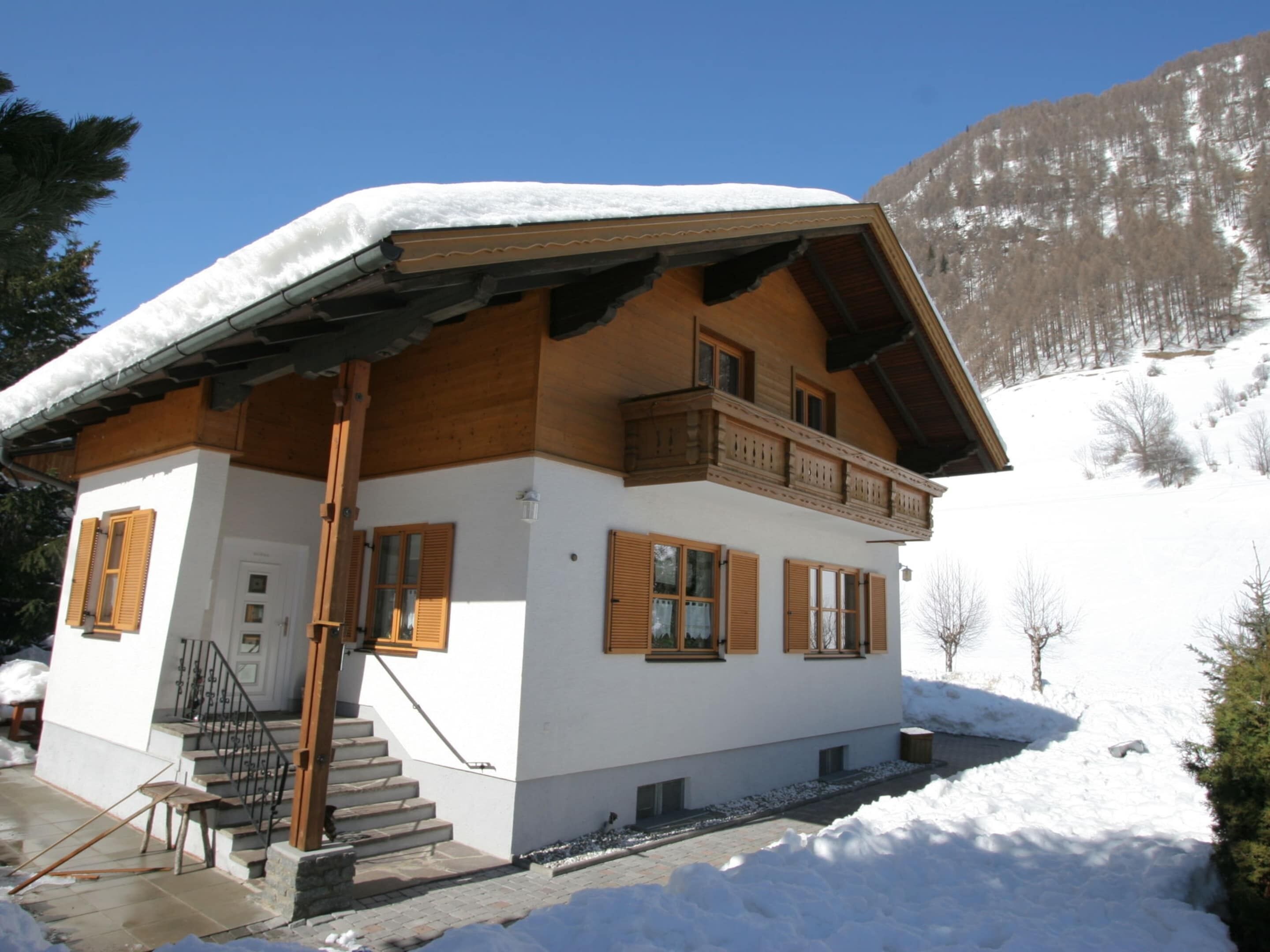 Eine zweistöckige Chalet mit Holzbalkon, weißen Außenwänden und einem mit Schnee bedeckten Dach.