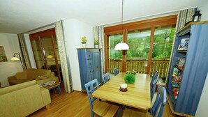 A cozy living room with a wooden dining table, blue chairs, a sofa, and a bookshelf. - Vibrant Apartment near Ski Slopes in Brand (Brand)