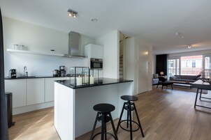 Una cocina moderna con una isla central, taburetes de bar y una escalera que conduce a un nivel superior.
