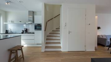 A modern kitchen with white cabinets, a wooden bench, and a staircase leading to another room.
