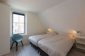 A bedroom with two beds, a window, a chair, and bedside lamps.