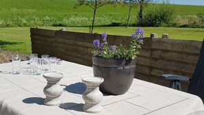 An outdoor table set with glasses and a potted plant, surrounded by a wooden fence and a green field. - Cosy Holiday Home With Large Garden (Zonnemaire)