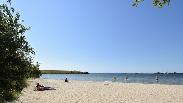 A sandy beach with people sunbathing and swimming. - Cosy Holiday Home With Large Garden (Zonnemaire)