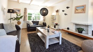 A modern living room with a black leather sofa, a white coffee table, and a fireplace. - Cosy Holiday Home With Large Garden (Zonnemaire)