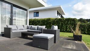 A modern outdoor patio with a grey sectional sofa and ottoman, a small table, and a potted plant. - Holiday Home in Harderwijk Near Serene Lake (Zeewolde)